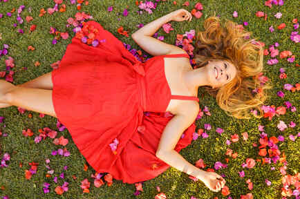 Mujer en vestido rojo, acostada sobre flores de primavera