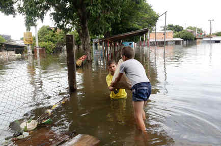 Marino Gomez entrega un saco de comida a su hermano Pablo en una zona inundada del vecindario Bañado Norte, en Asunción, Paraguay, el domingo 27 de diciembre de 2015. 