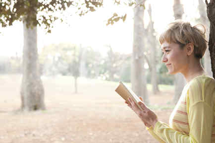 Mujer rubia leyendo junto a un árbol