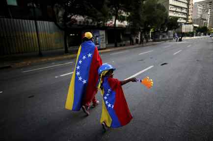 Un manifestante contrario al gobierno y su hija, envueltos en banderas de Venezuela, caminan por una calle desierta de Caracas, Venezuela, el domingo 30 de julio de 2017. 