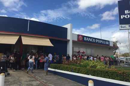Vista de una de las pocas sucursales bancarias abiertas en Puerto Rico. En la imagen numerosas personas hacen fila en una oficina de Banco Popular abierta en San Juan.