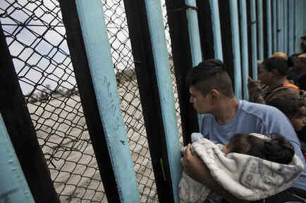 Migrantes centroamericanos sentados este domingo en el cerco fronterizo, cerca del mar, en San Diego, California. 