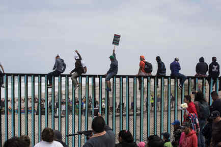 Inmigrantes de la caravana centroamericana se sientan en muro de frontera con México