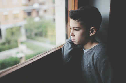 Niño triste mirando por la ventana