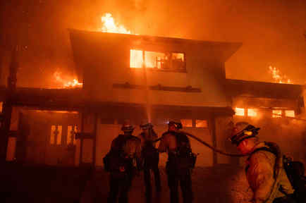 Bomberos frente a una vivienda que está siendo consumida por las llamas en el sur de California