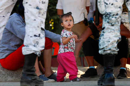 Una niña en la frontera entre México y Estados Unidos junto a su mamá rodeada de agentes.