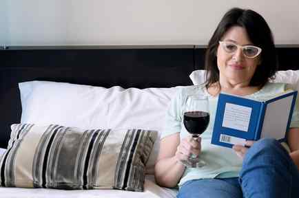 Mujer recostada en la cama leyendo y bebiendo vino tinto