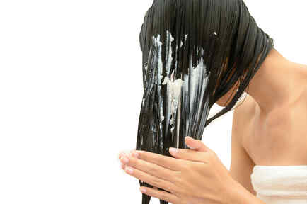 mujer con cabello negro aplicándose un producto en el pelo