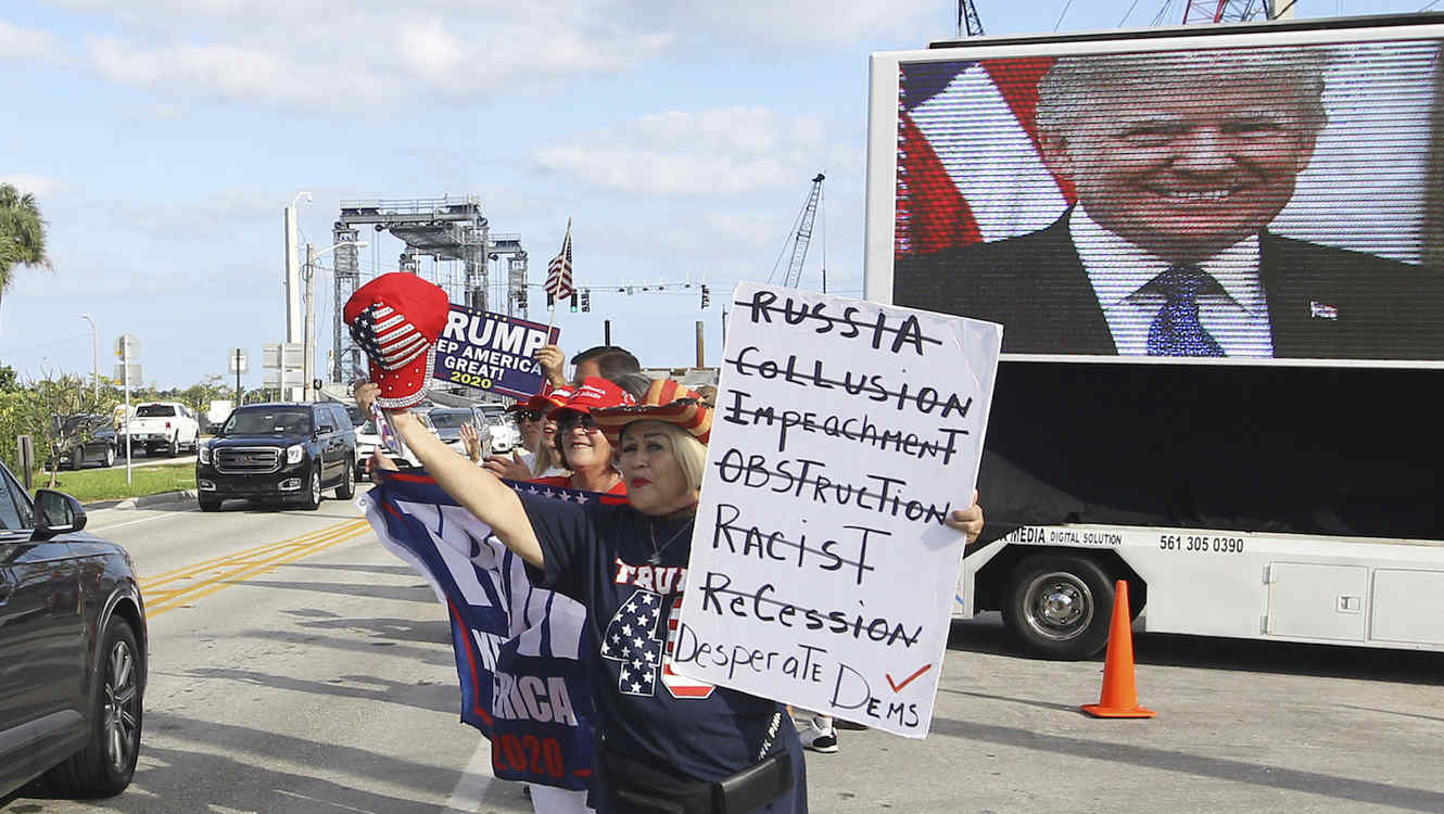 Un grupo de personas espera con carteles de apoyo el paso del vehículo de Trump en su residencia de Mar-a-Lago (Florida) este domingo.  