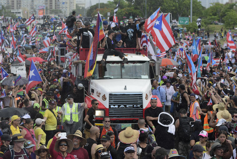 El cantante puertorriqueño Ricky Martin, al frente en el techo del camión, participa con otras celebridades locales en una protesta para exigir la renuncia del gobernador Ricardo Rosselló, en San Juan, Puerto Rico, el lunes 22 de julio de 2019.