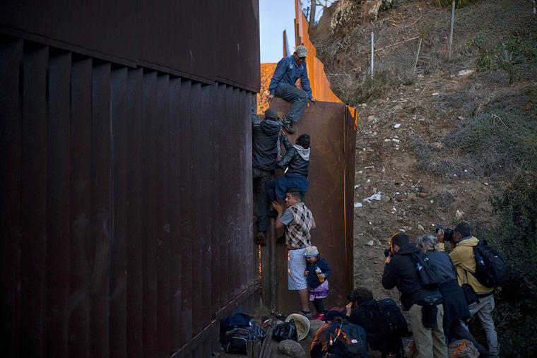 Un migrante hondureño ayuda a otros a cruzar el muro entre México y Estdos Unidos. 