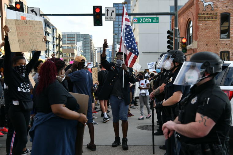 Un hombre afroamericano sostiene una bandera mientras los manifestantes se enfrentan con oficiales de la policía de Denver, Colorado, este jueves en la noche.