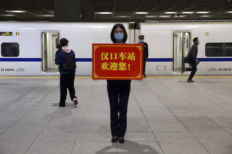 Una trabajadora ferroviaria sostiene un cartel que dice "¡La estación Hankou te da la bienvenida!", mientras los pasajeros abordan el primer tren de alta velocidad que sale de la estación de Hankou después de la reanudación de los servicios de trenes en W