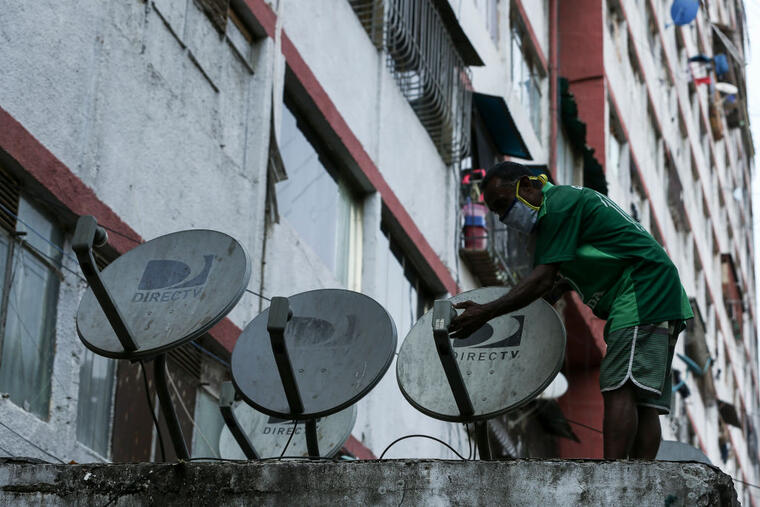 Un hombre con tapaboca examina una antena de DirectTV en un edificio humilde de Caracas el pasado martes 19 de mayo, luego de que la cableoperadora anunciara su retiro de Venezuela.