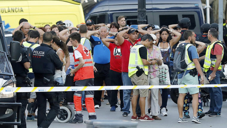 Un grupo de gente con los brazos en alto ante el despliegue policial en el lugar del atentado ocurrido hoy en las Ramblas de Barcelona