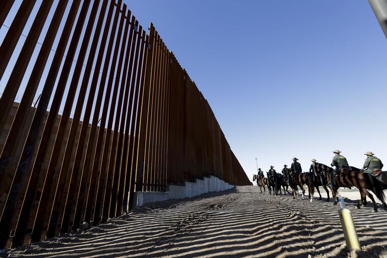 Agentes de la Patrulla Fronteriza montados viajan a lo largo de una estructura de muro fronterizo reforzada
