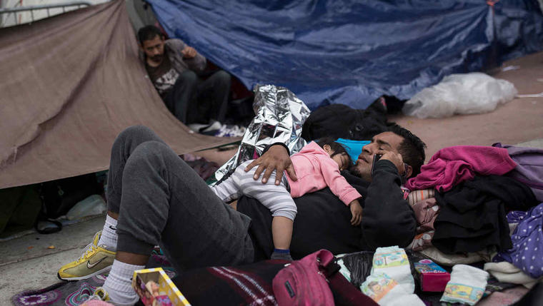 Un hombre con una niña en sus brazos de la caravana de inmigrantes en la frontera con EEUU.