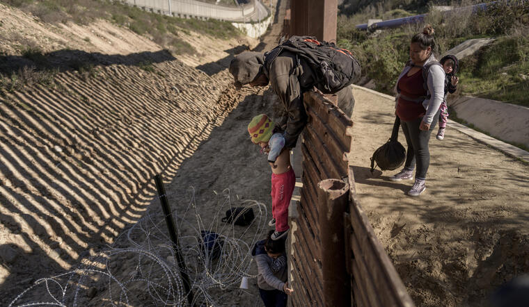 Un hombre pasa a un bebé mexicano a su madre tras saltar la valla fronteriza cerca de Tijuana.  