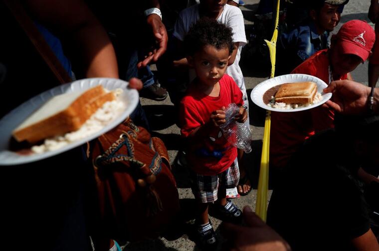 Migrantes centroamericanos almuerzan este domingo, cortesía de las autoridades mexicanas, mientras esperan que se procesen sus visas humanitarias en un puente fronterizo entre México y Guatemala.