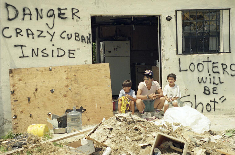 Orlando Somante, sentado el 27 de agosto de 1992 con sus hijos a la entrada de su casa en Cutler Ridge. En la pared, dos mensaje: "Se disparará a los ladrones", y "Peligroso cubano loco dentro". 