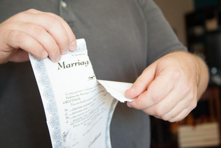 Un hombre rompiendo un certificado de matrimonio por la mitad.