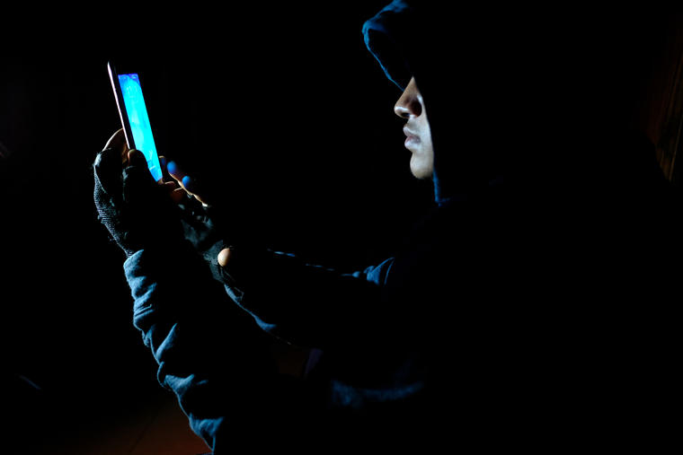 Hooded hacker stealing perdonal data or bank information using smart phone