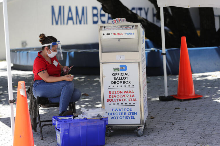 Una trabajadora de las urnas en Florida usa una mascarilla mientras vigila un buzón en el que los votantes depositan sus papeletas por correo