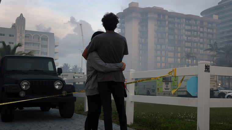 Dos personas se consuelan mutuamente mientras miran el edificio de condominios Champlain Towers South de 12 pisos derrumbado el 25 de junio de 2021 en Surfside, Florida.