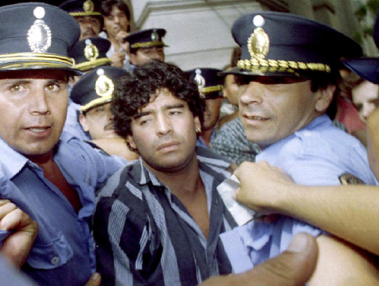 Maradona escoltado por la policía al salir de un juzgado, tras responder a cargos por disparar y herir a periodistas afuera de su casa de campo dos meses antes, en la ciudad de Mercedes a las afueras de Buenos Aires, el 15 de marzo de 1994.