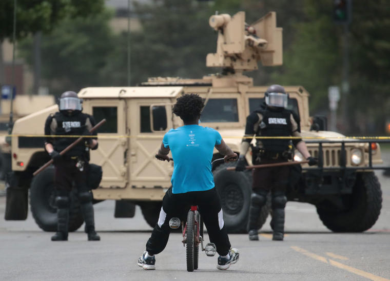 Un hombre afroamericano monta una bicicleta este 29 de mayo hasta el puesto de control de la policía después de que la ciudad sufriera una noche de protestas y violencia.