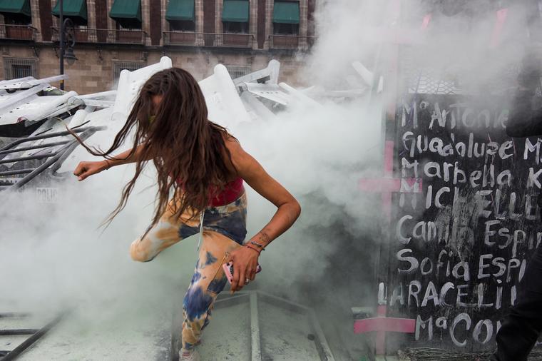 Una mujer corría en medio de los gases lacrimógenos, lanzados por los cuerpos policiales, frente al Palacio Nacional, en Ciudad de México, el 8 de marzo de 2021.