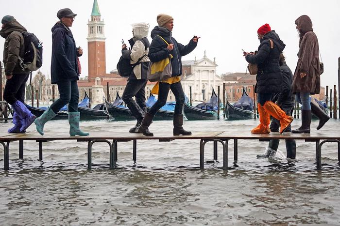 Transeúntes cruzan este martes una zona inundada de Venecia por encima de varios bancos.