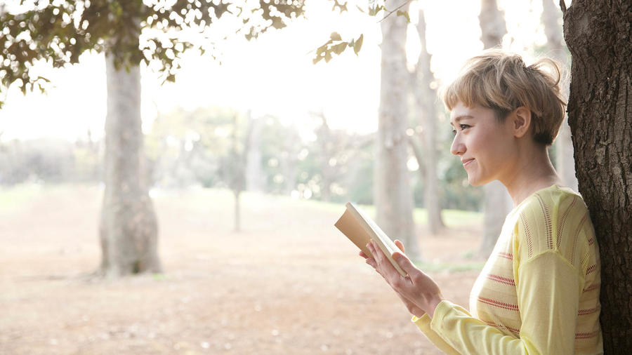 Mujer rubia leyendo junto a un árbol