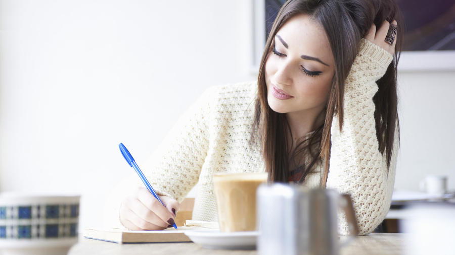 Mujer joven escribiendo y bebiendo café
