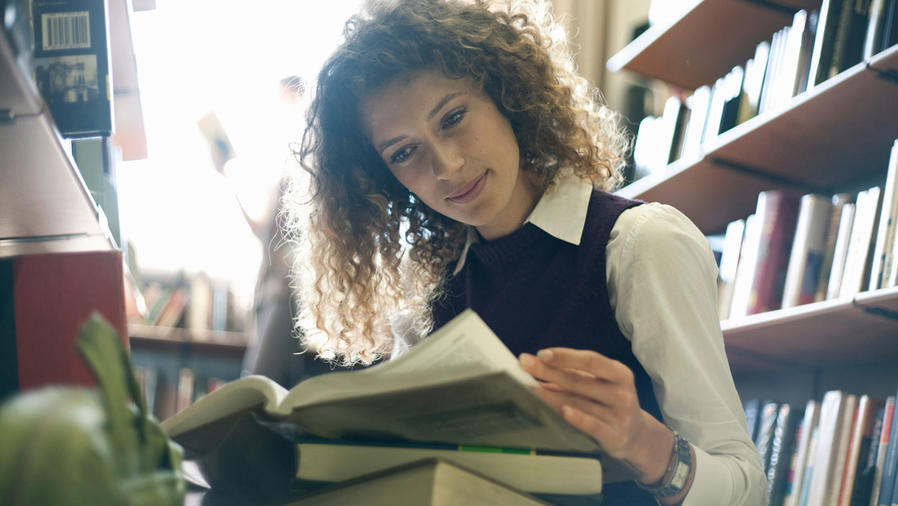 Mujer joven leyendo libros en la biblioteca
