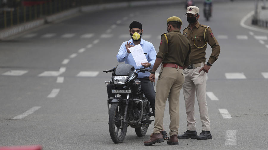 Un hombre en motocicleta muestra sus papeles a dos policías durante la cuarentena en Jammu, India.