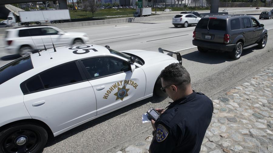 En esta imagen del 23 de abril de 2021, el oficial de la Patrulla de Caminos de California Troy Christensen revisa una licencia de conducir después de detener a un automovilista en la Interestatal 5 que conducía a exceso de velocidad en Anaheim, Californi