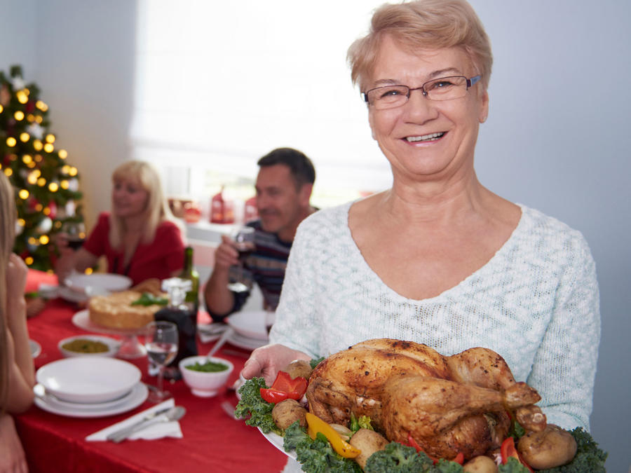 Abuela enseñando una bandeja con pollo durante cena navideña