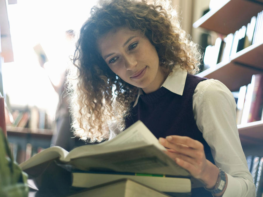 Mujer joven leyendo libros en la biblioteca
