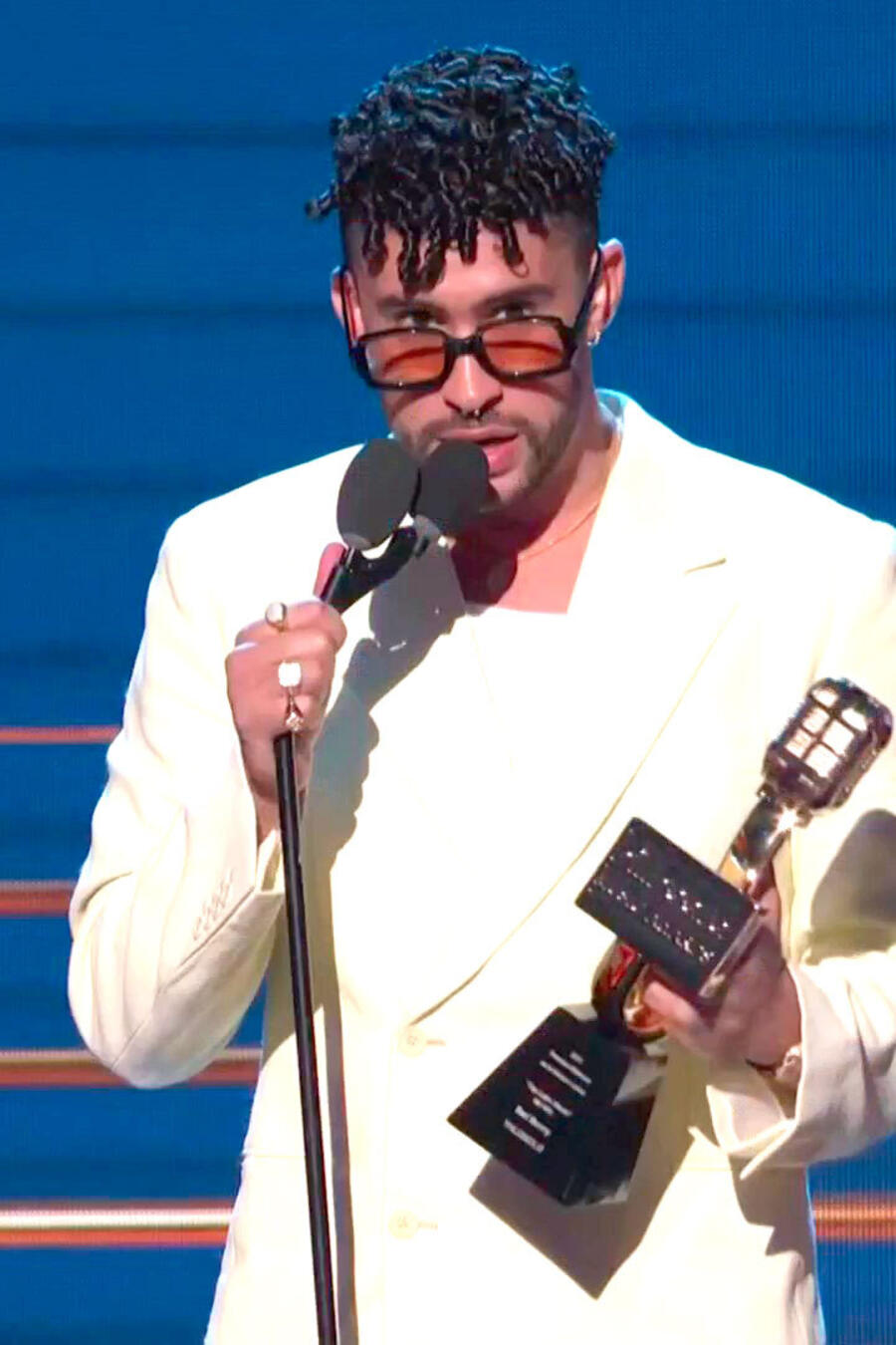 Bad Bunny acepta su premio a "Top Latin Album del Año" durante los Premios Billbaord 2021 en el Watsco Center de Miami, Florida el 23 de septiembre en el vistiendo una traje satinado de color blanco, camiseta blanca, gafas de sol de marco negro y zapatos 